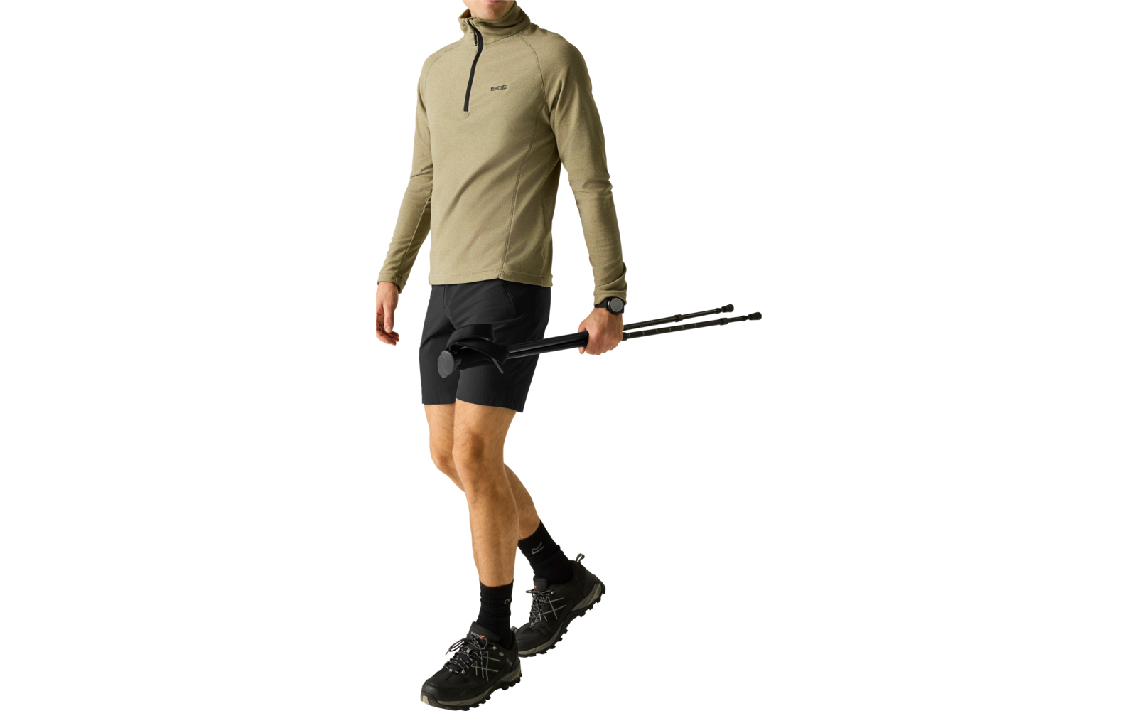 Person mit beigefarbenem Langarm-Oberteil mit kurzem Reißverschluss, schwarzen Shorts und schwarzen Wanderschuhen, hält zusammengeklappte Trekkingstöcke in einer Hand