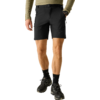 Unterkörper einer stehenden Person mit olivgrünem Langarmshirt, schwarzen Shorts mit schwarzem Gürtel, einer schwarzen Armbanduhr, schwarzen Socken und schwarzen Wanderschuhen