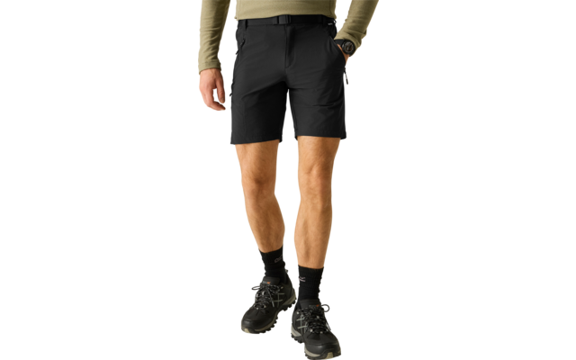 Unterkörper einer stehenden Person mit olivgrünem Langarmshirt, schwarzen Shorts mit schwarzem Gürtel, einer schwarzen Armbanduhr, schwarzen Socken und schwarzen Wanderschuhen