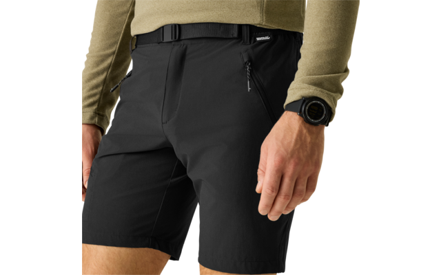 Unterer Torso einer Person mit schwarzen Shorts mit Reißverschlusstaschen und Gürtel, olivgrüner Langarmpullover, sichtbare Hände, linkes Handgelenk mit schwarzer Smartwatch