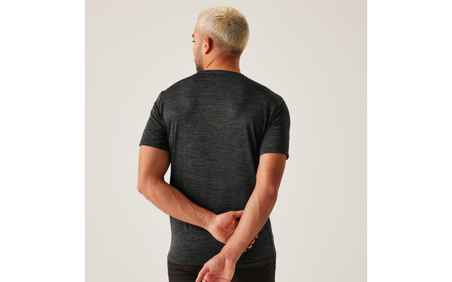 Rückansicht einer Person mit kurzgeschorenem blondem Haar, dunkelgrauem T‑Shirt mit kurzen Ärmeln, Hände hinter dem Rücken zusammengeführt, heller Hintergrund