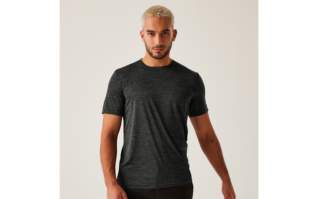 Mann mit kurz blondiertem Haar und kurzem Bart, trägt dunkelgraues meliertes T‑Shirt, steht vor hellem Hintergrund, Arme seitlich, kleines schwarzes Tattoo am inneren rechten Unterarm