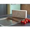 Altavoz portátil rectangular beige sobre encimera de cocina junto a tomates cherry y un fregadero