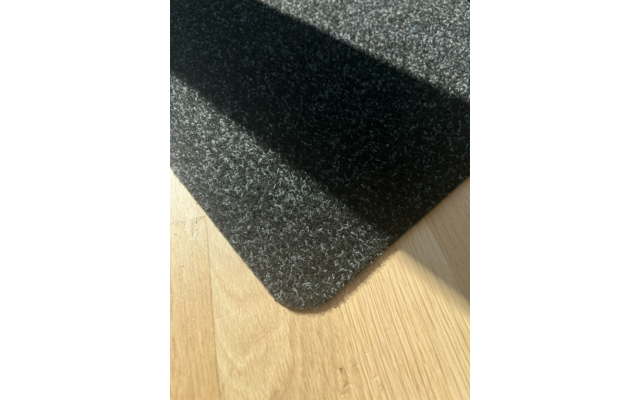 Dunkelgraue Filzmatte mit abgerundeter Ecke auf hellem Holzfußboden, diagonaler Schatten