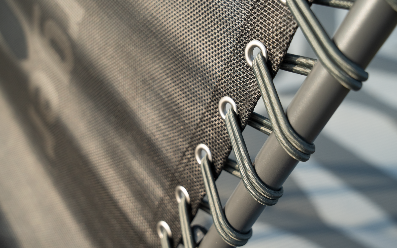 Close-up van donker meshstof met metalen ringen en elastische koorden die om grijze metalen buizen zijn geleid