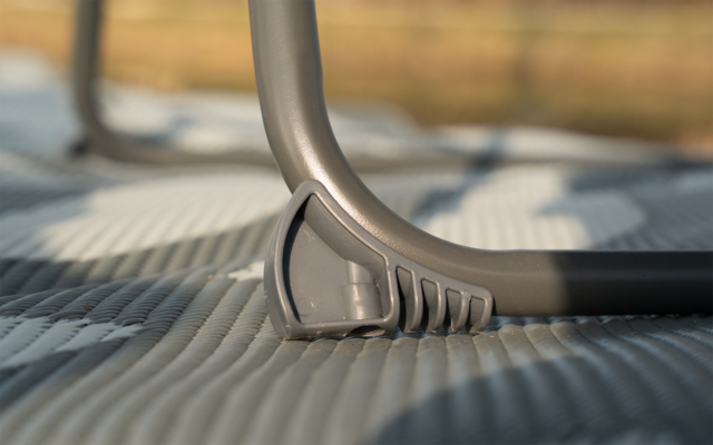 Close-up van een grijs, gebogen metalen frame met een kunststof voet op een geribbelde mat; onscherpe achtergrond