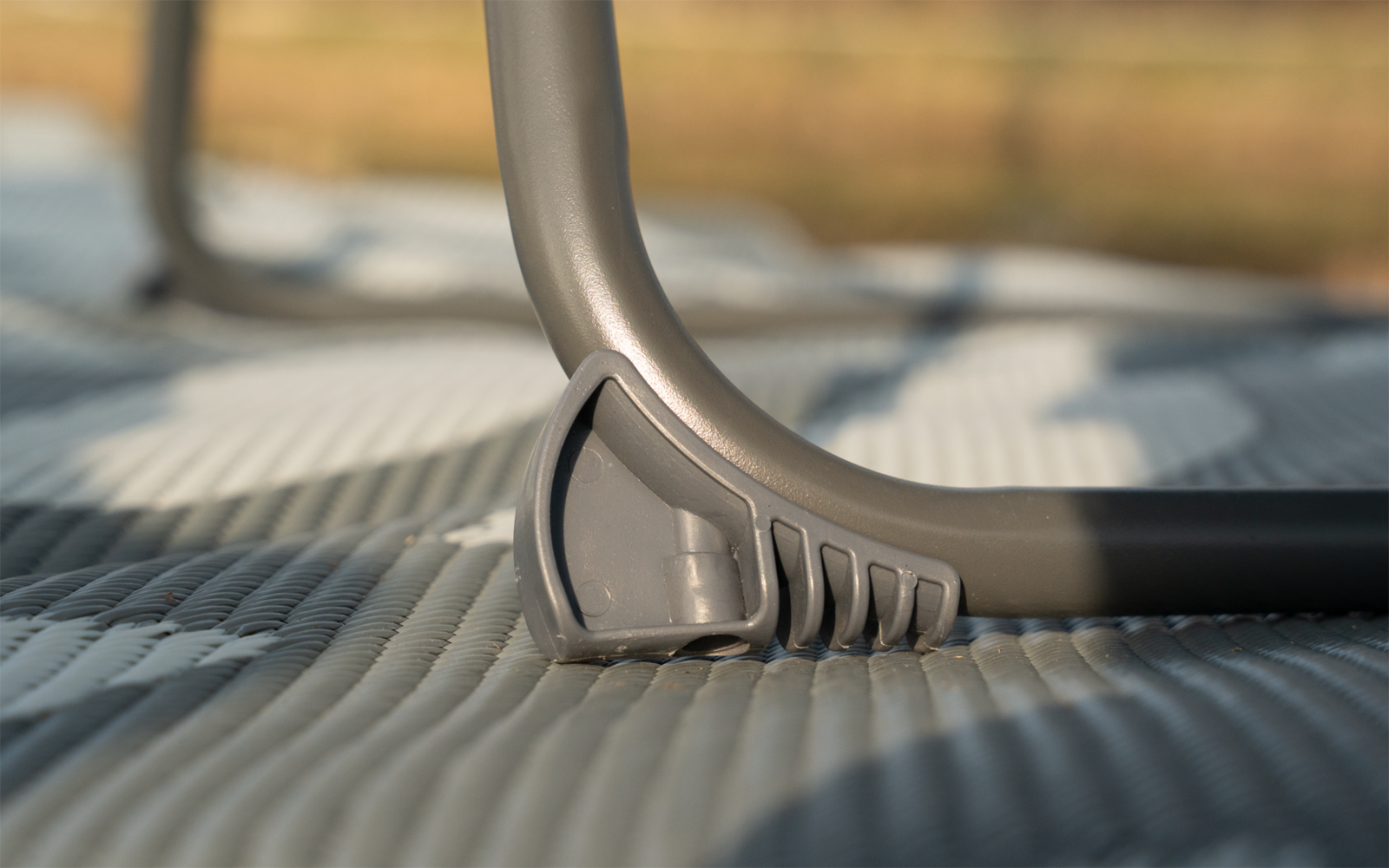 Close-up van een grijs, gebogen metalen frame met een kunststof voet op een geribbelde mat; onscherpe achtergrond