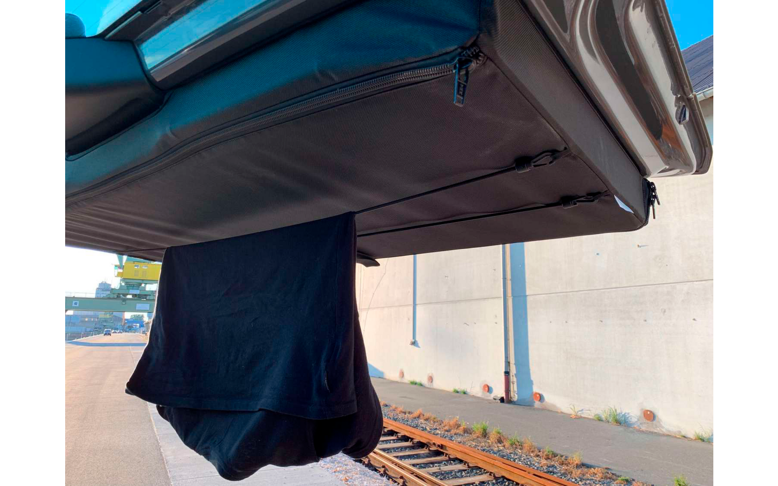 Prenda negra colgada en la puerta trasera abierta de un vehículo, con vías y una pared de hormigón al fondo