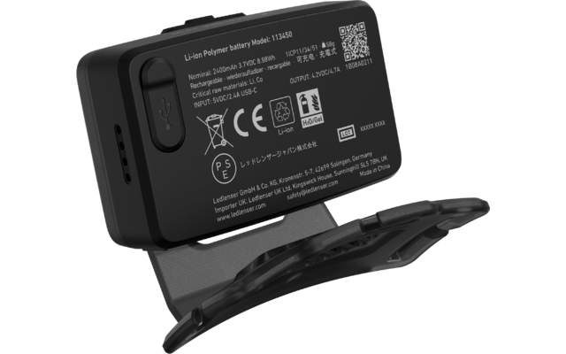 Schwarzes rechteckiges Gehäuse mit weißen Aufdrucken und Prüfsymbolen, QR‑Code, gummierter USB‑Abdeckung an der Seite und grauem klappbarem Standfuß/Clip vorne