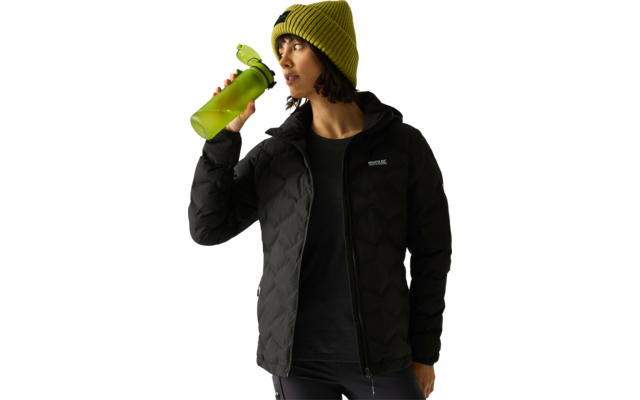 Persona con berretto verde a maglia e giacca imbottita nera tiene una borraccia verde vicino alla bocca e guarda verso destra su uno sfondo chiaro e uniforme