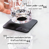 Hand hält ein durchsichtiges Glas über einem quadratischen schwarzen Lederuntersetzer auf weißer Marmoroberfläche