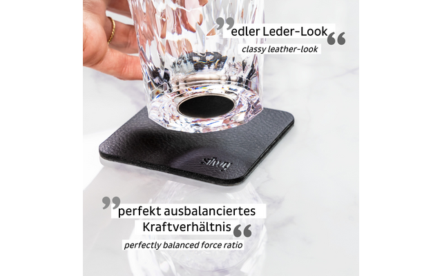 Hand hält ein durchsichtiges Glas über einem quadratischen schwarzen Lederuntersetzer auf weißer Marmoroberfläche
