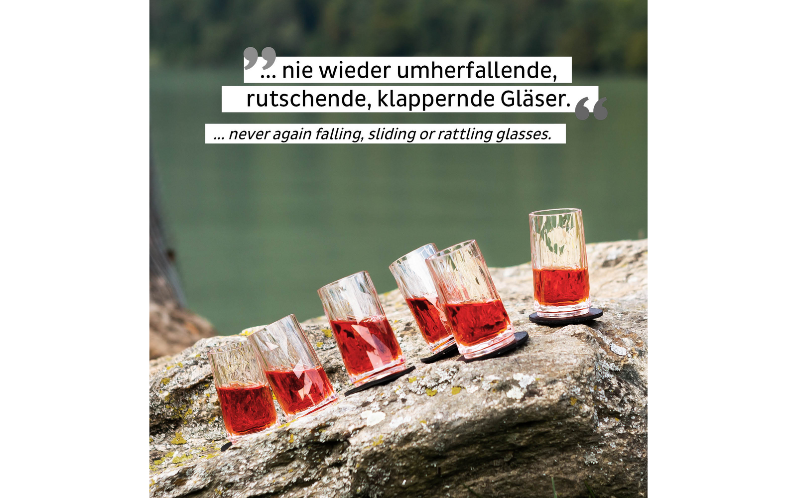 Sechs Gläser mit rotem Getränk stehen und kippen auf einem Stein am Wasser