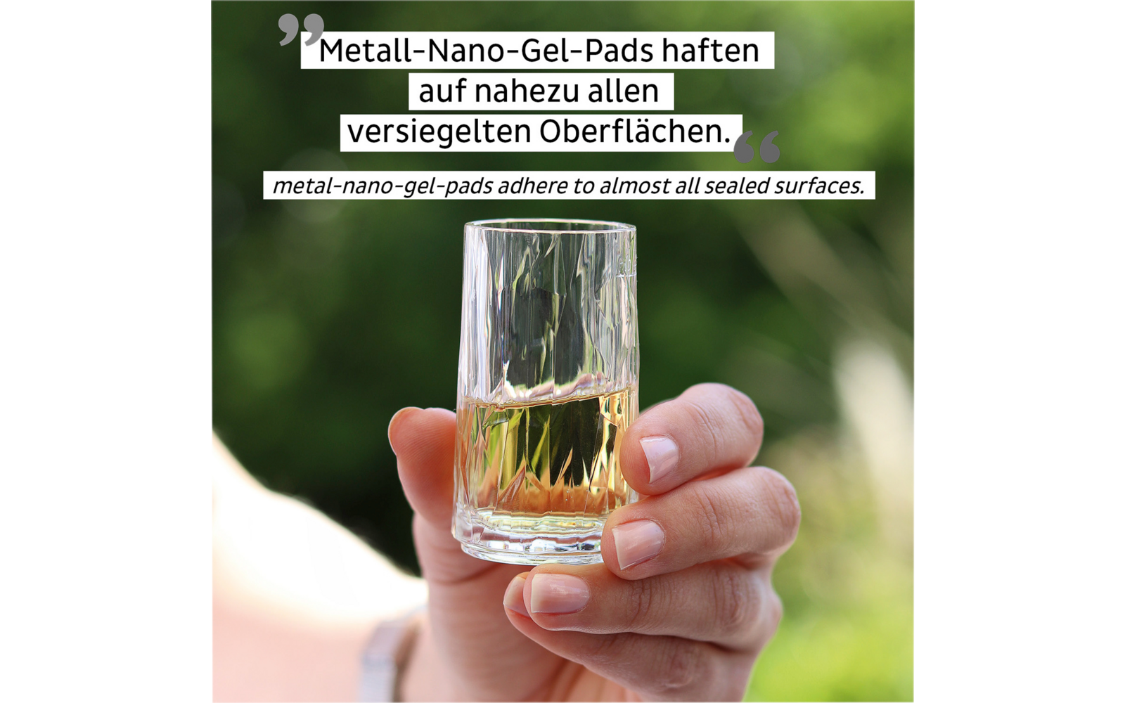 Hand hält ein klares Glas mit Flüssigkeit vor unscharf grünem Hintergrund
