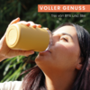 Nahaufnahme einer Person, die einen gelben Trinkbecher zum Mund führt, Kopf nach hinten geneigt; grüne Pflanzen im Hintergrund; orangenes Banner mit dem Text 'VOLLER GENUSS' und kleiner weißer Schrift 'frei von BPA und Blei'