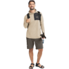 Stehender Mann, beiger Kapuzenpullover mit schwarzer Brusttasche, dunkelgraue Shorts, schwarzer Rucksack, schwarze Sandalen, hält in der rechten Hand ein schwarzes Objekt mit blauem Detail