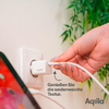 Hand steckt USB-Stick in einen USB-Adapter an einer Wandsteckdose, im Hintergrund eine Pflanze