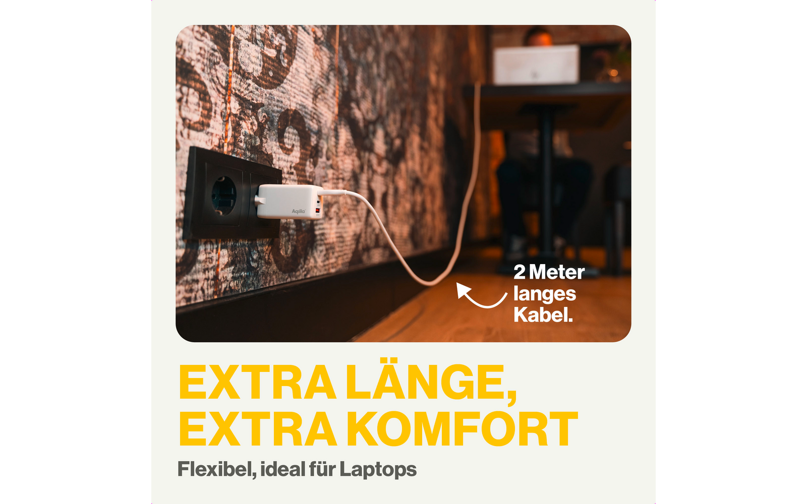 Ein Laptop lädt über ein weißes USB-Kabel an einer Steckdose mit rauer Wand, rechts ein Stuhl