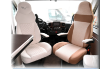 Twee leren stoelen in een voertuig, één wit en één beige, met armleuningen en dashboard op de achtergrond