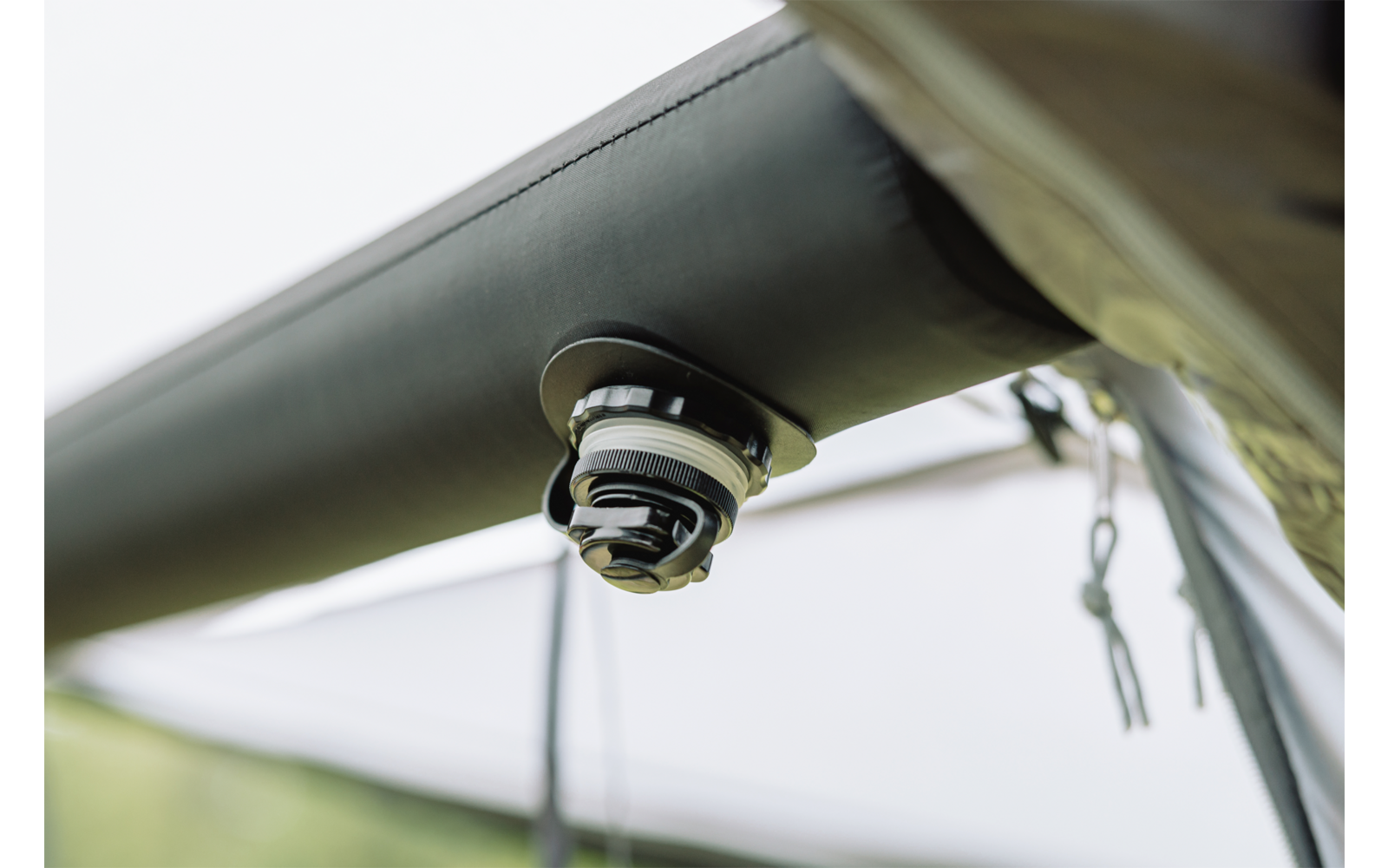 Close-up van een rond plastic- en metalen onderdeel bevestigd aan een donkere buis onder licht textiel
