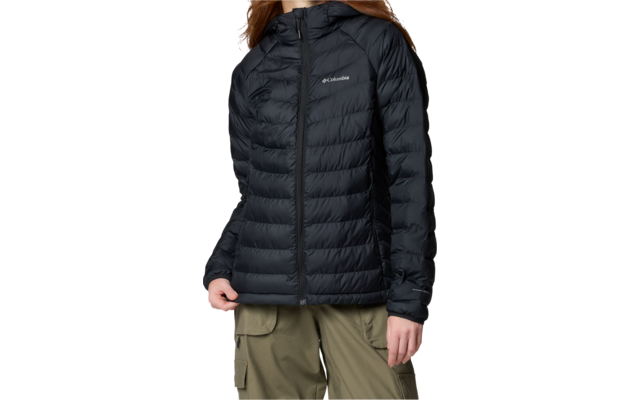 Personne sur fond blanc, porte une doudoune noire matelassée à capuche avec fermeture éclair et logo Columbia, pantalon cargo olive, cheveux mi-longs châtain-roux