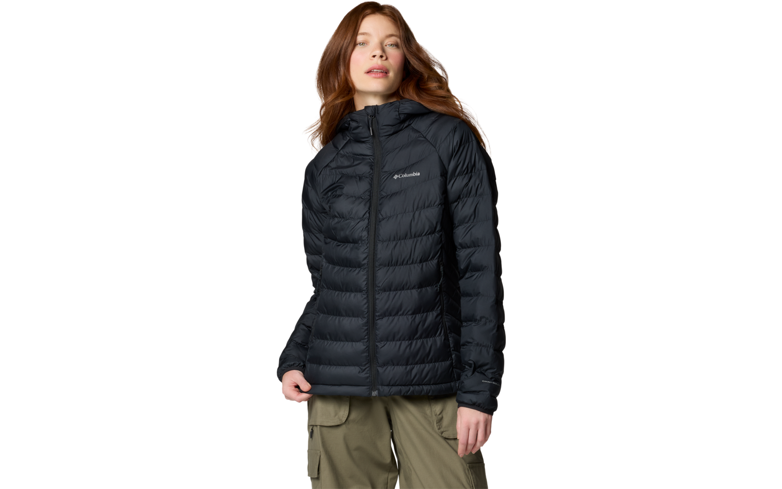 Personne sur fond blanc, porte une doudoune noire matelassée à capuche avec fermeture éclair et logo Columbia, pantalon cargo olive, cheveux mi-longs châtain-roux