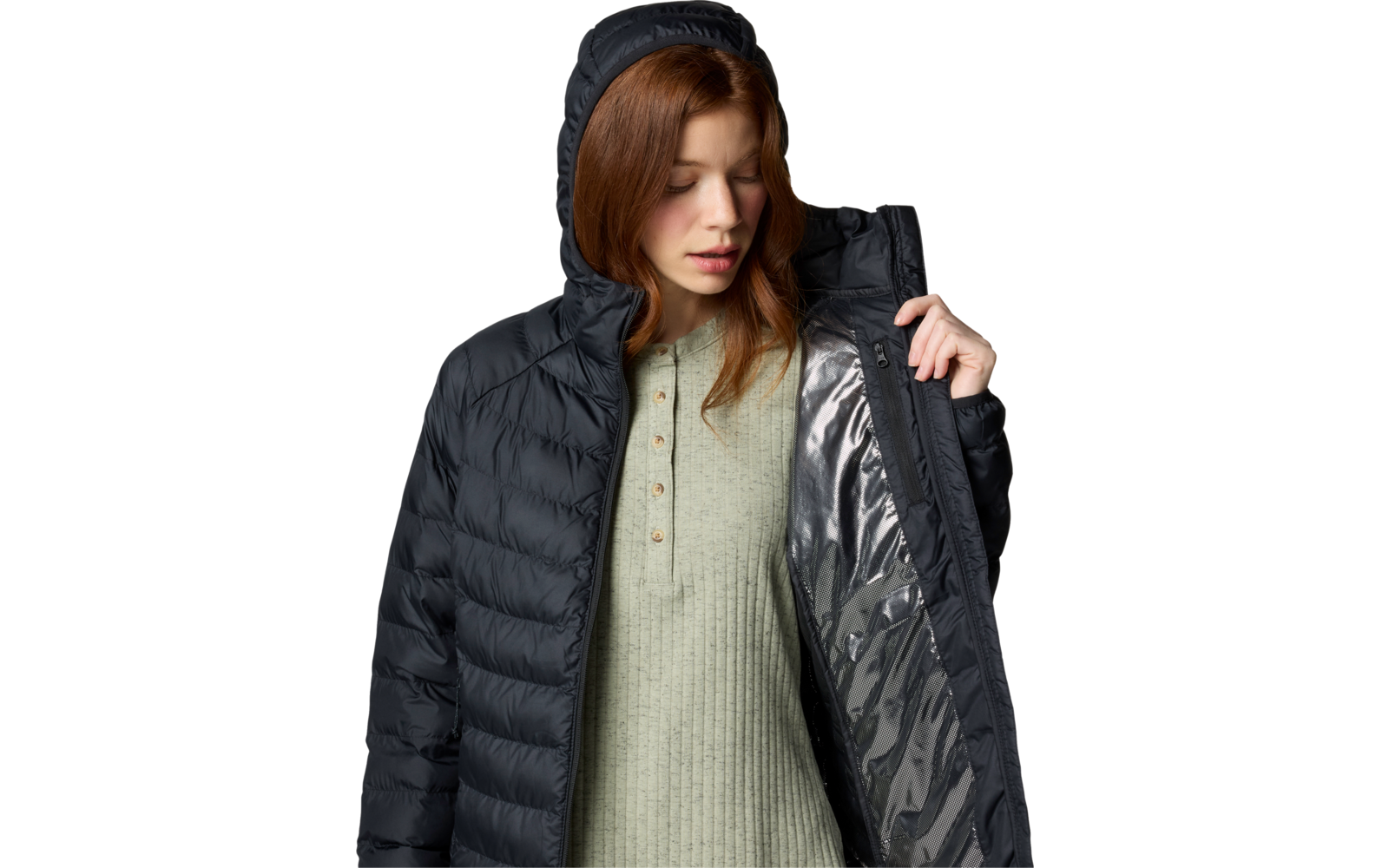 Femme aux cheveux roux portant une doudoune noire à capuche, tenant la veste ouverte ; pull vert en maille avec patte de boutons visible