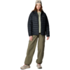 Personne debout de face portant un bonnet beige avec inscription, une doudoune noire matelassée, un pull zippé vert clair, un pantalon cargo vert olive et des baskets beiges; cheveux bruns mi-longs; fond blanc