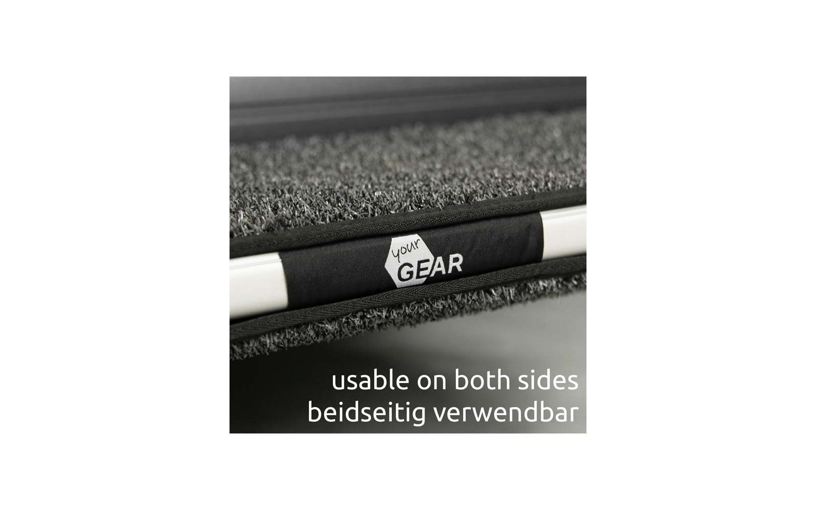 Nahaufnahme einer grauen, strukturierten Matte mit schwarzem Riemen, weißem Sechseck-Logo 'your GEAR' auf dem Riemen und einer weißen Stange; unten der Text 'usable on both sides beidseitig verwendbar'