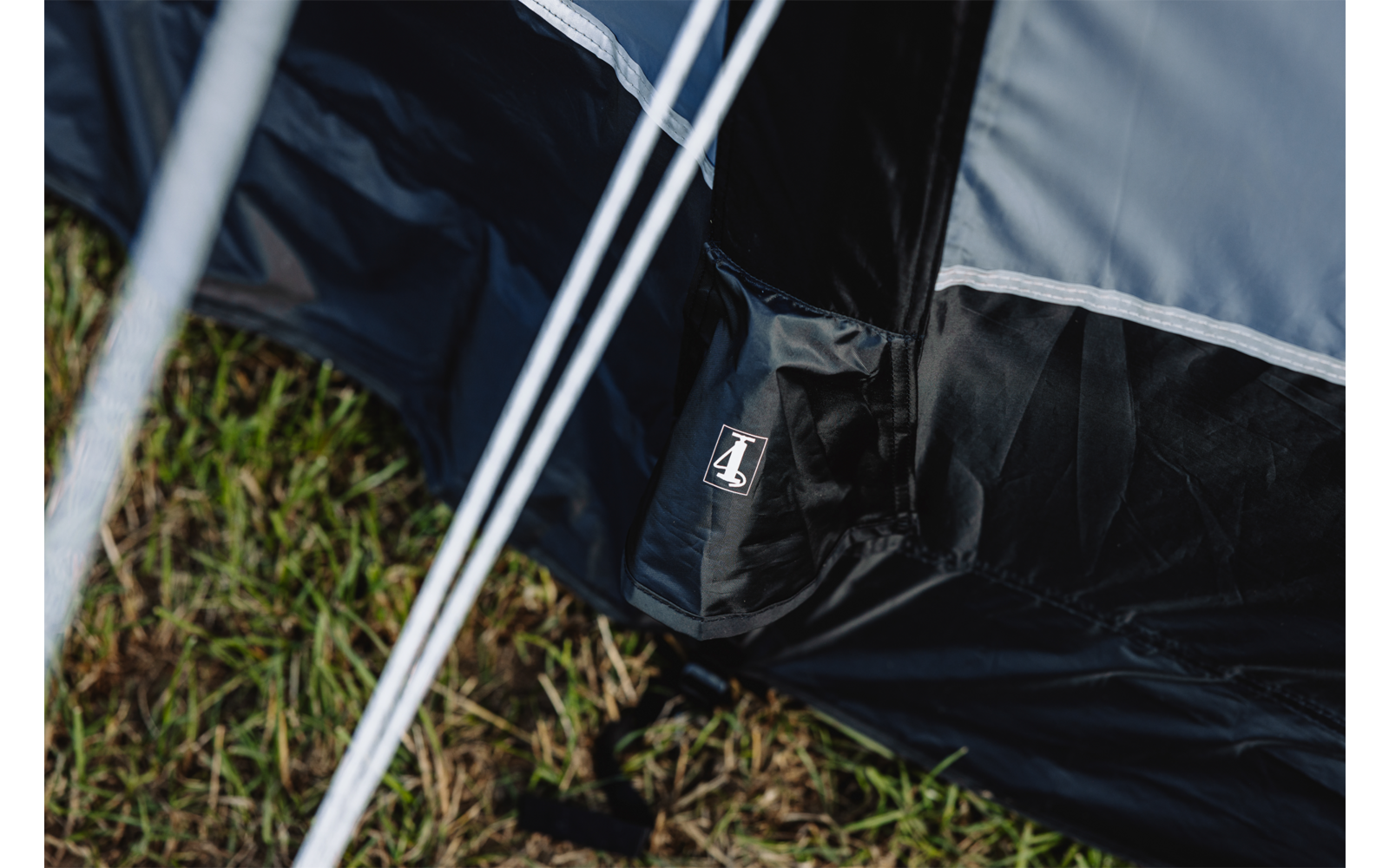 Nahaufnahme von dunklem Zeltstoff mit kleinem weißem Logo-Etikett, Zeltstangen und Gras