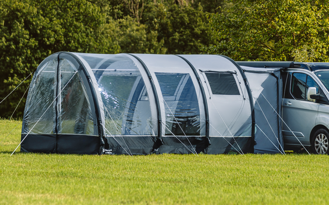 Weißer Van neben großem grauem Tunnelzelt auf einer Wiese, im Hintergrund Bäume