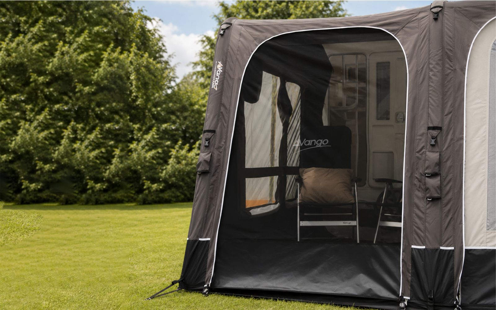 Donkergrijze voortent met open ingang, binnen twee campingstoelen met kussen, groen gras en bomen op de achtergrond