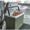 Glacière portable vert olive avec couvercle ouvert, poignée noire rabattable et intérieur blanc ; deux bouteilles de boisson orange à l'intérieur ; jerrican blanc et paroi en tissu gris en arrière-plan