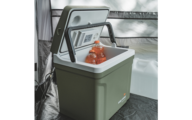 Glacière portable vert olive avec couvercle ouvert, poignée noire rabattable et intérieur blanc ; deux bouteilles de boisson orange à l'intérieur ; jerrican blanc et paroi en tissu gris en arrière-plan