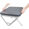 Two hands hold a gray padded square seat cover with a zipper and visible logo; below it a black crossed metal frame of a folding stool