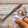 Auf einer Holzoberfläche liegt ein gezahntes Brotmesser mit rotem und schwarzem Griff, daneben zwei Baguettes in einem blau karierten Tuch, eine Glasflasche Olivenöl und einige Ähren