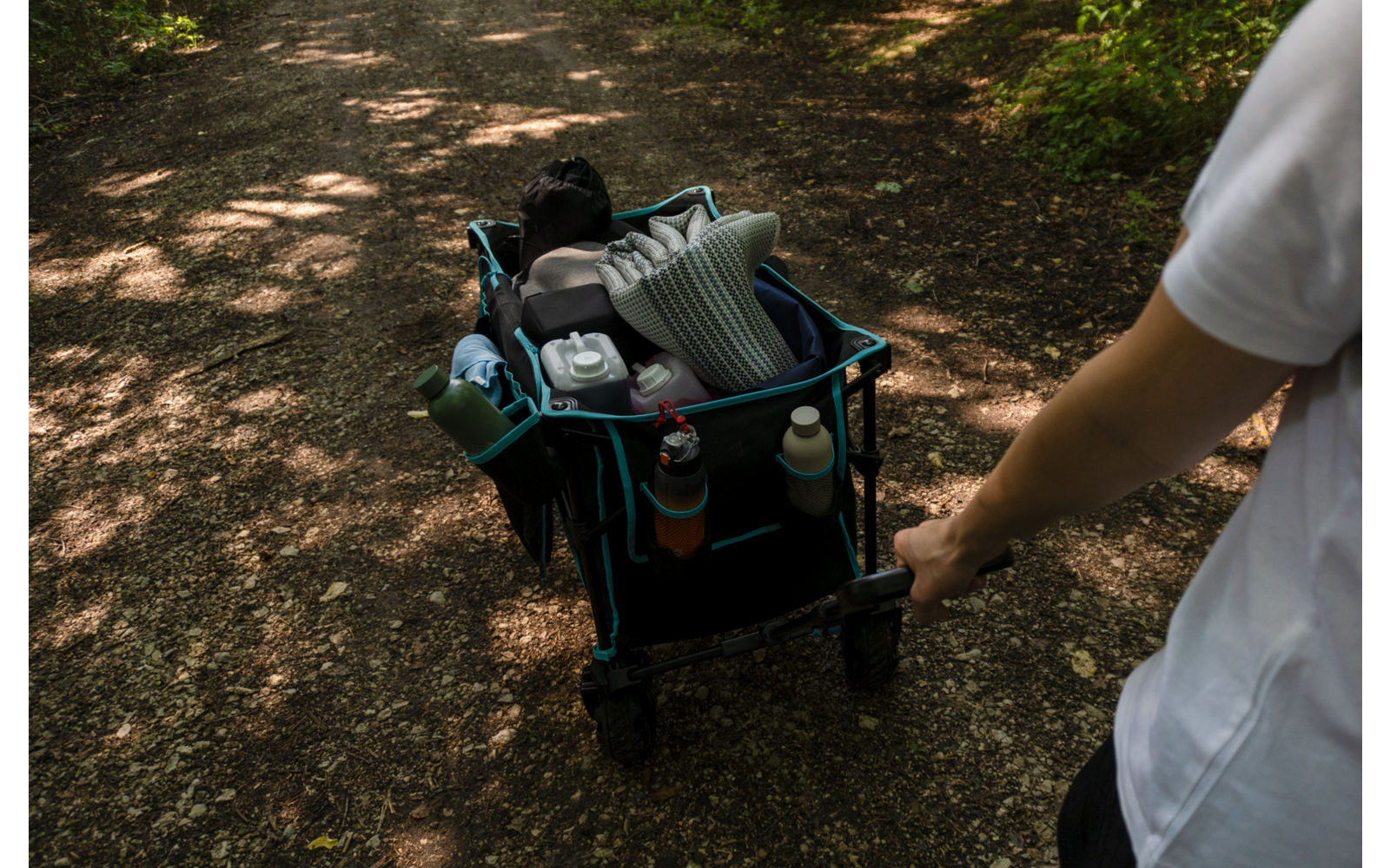 Eine Person hält den Griff eines Kinderwagens im Wald auf einem schattigen Weg