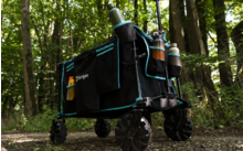 Carro plegable negro con dos botellas, situado en un sendero del bosque