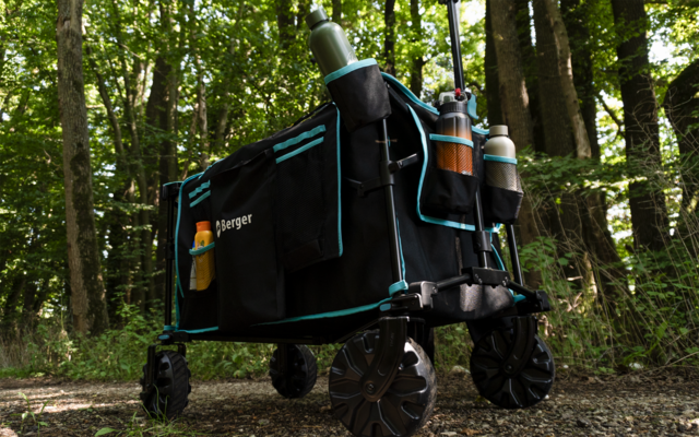 Schwarzer klappbarer Wagen mit zwei Flaschen, steht auf einem Waldweg