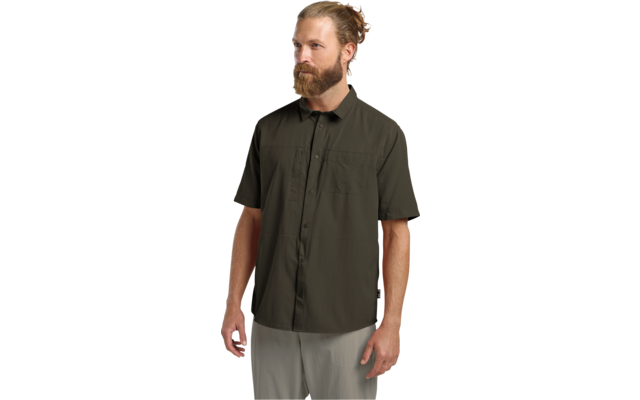 Mann mit Bart und Dutt trägt olivgrünes kurzärmeliges Hemd mit Knöpfen und helle Hose, steht und blickt nach links
