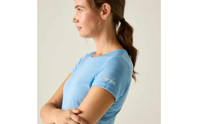 Zijaanzicht van een persoon die naar links kijkt met gekruiste armen, een lichtblauw T-shirt met korte mouwen en een lage paardenstaart voor een beige achtergrond