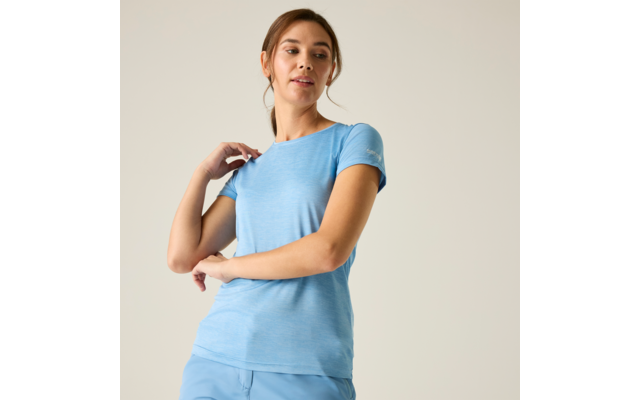 Persoon in lichtblauw T-shirt en blauwe broek voor een effen achtergrond, één hand op de schouder, kijkt zijwaarts