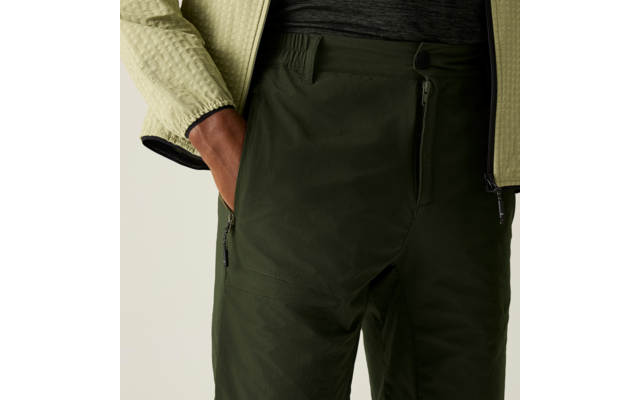 Nahaufnahme der Hüfte und Oberschenkel einer Person, dunkelgrüne Hose mit Reißverschlusstaschen, linke Hand in der Tasche, hellgrüne strukturierte Jacke