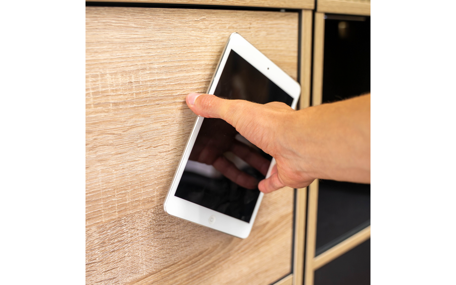 Hand hält ein weißes Tablet mit schwarzem Bildschirm zwischen zwei Schubladen eines hellen Holzschranks