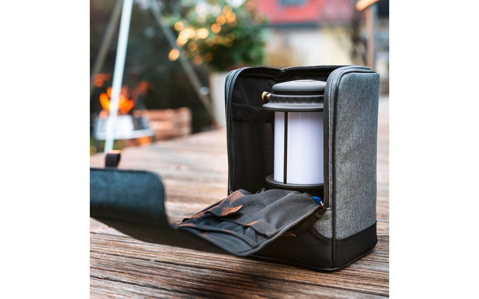Custodia in tessuto grigio aperta con una lanterna portatile cilindrica bianca su un tavolo di legno; fuoco aperto sfocato sullo sfondo