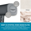 Nahaufnahme eines grauen Dampfbügel-/Glätterkopfs mit keramisch beschichteter Platte, zwei grauen Rundetiketten mit "CERAMIC COATING" und "AREA SIZE: 9 x 7 cm", rechts zwei Stoffproben mit den Beschriftungen "WOLLE" und "KASCHMIR", unten eine türkise