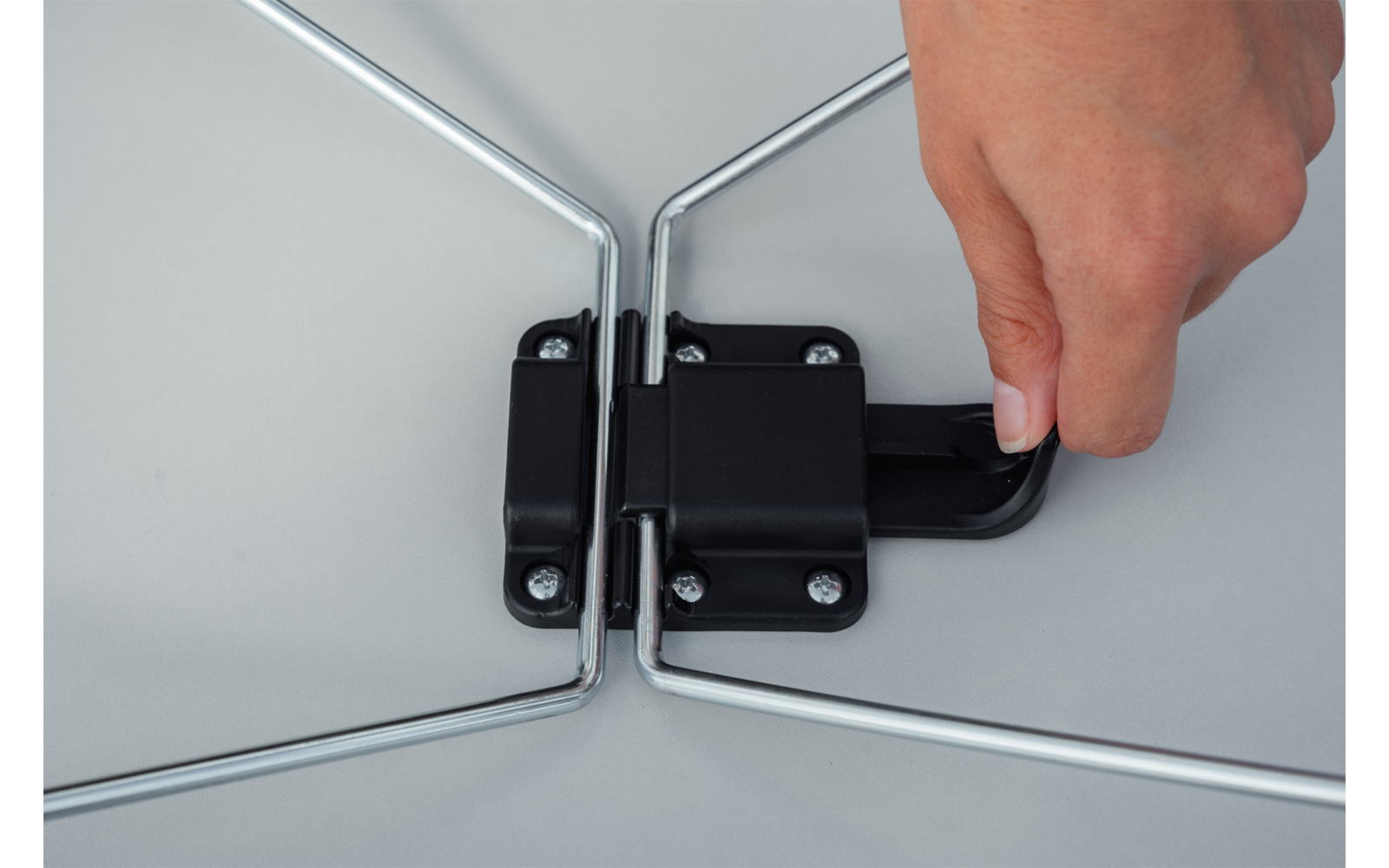 Close-up of a right hand holding a black plastic lever on a black hinge between two silver metal bars against a gray background