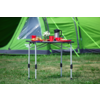 Een inklapbare campingtafel met koffiekopjes, een koffiekruik en een bord voor een groen tent op gras
