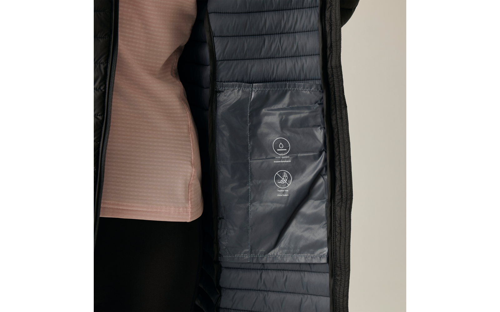 Interno di un cappotto trapuntato blu scuro aperto con tasca interna e due pittogrammi di cura bianchi; a sinistra top rosa chiaro parzialmente visibile e leggings neri, sfondo neutro