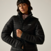 Donna con giacca imbottita nera trapuntata che tiene la cerniera, top rosa chiaro visibile al colletto, sfondo chiaro uniforme